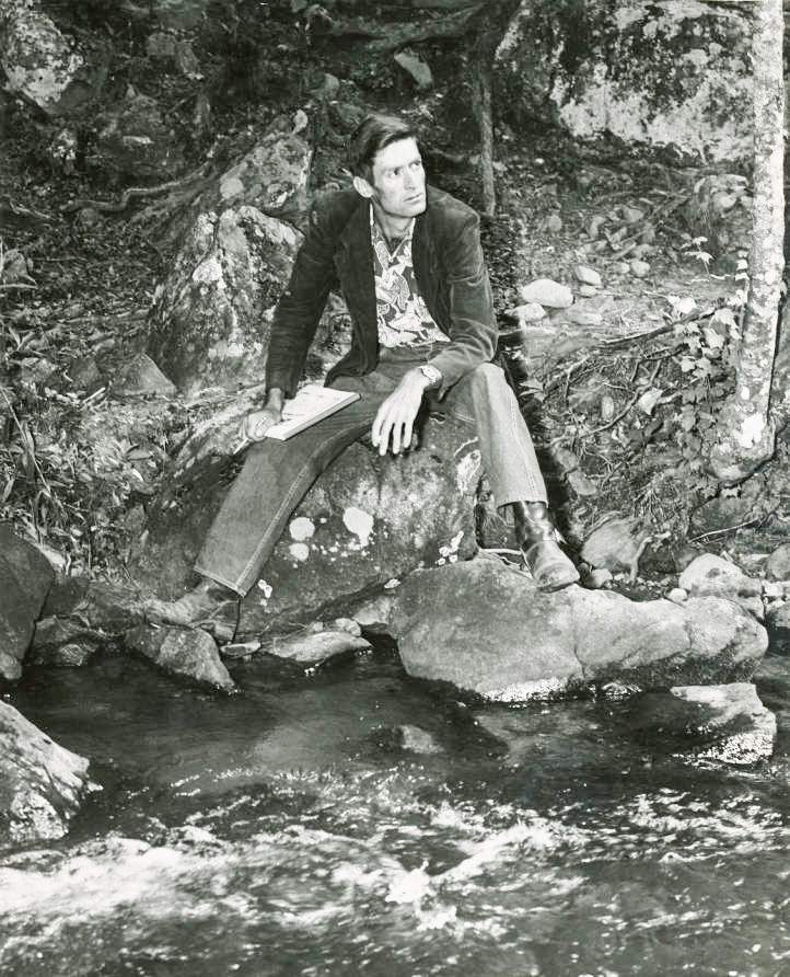 Poet Byron Herbert Reece sitting on the edge of a river withpaper and pencil in hand in the 1950s. AJC file