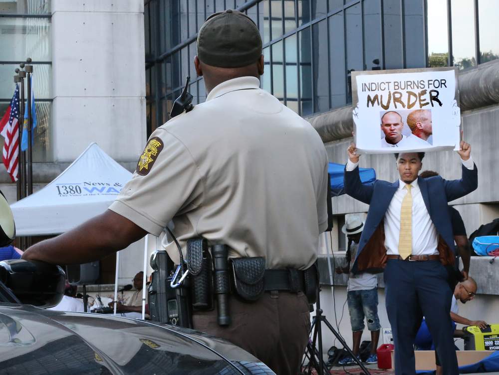 A Fulton County Sheriff&#39;s Deputy watches a protester seeking an indictment for murder during a protest around the convening of the Deravis Caine Rogers grand jury at the Fulton County Courthouse on August 30, 2016, in Atlanta. PHOTO: Curtis Compton \/ AJC