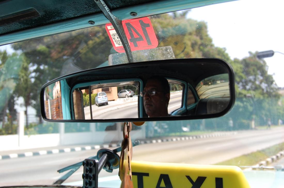 A Havana taxi driver is reflected in the rearview mirror of his cab.Photo: Katie Leslie / kleslie@ajc.com