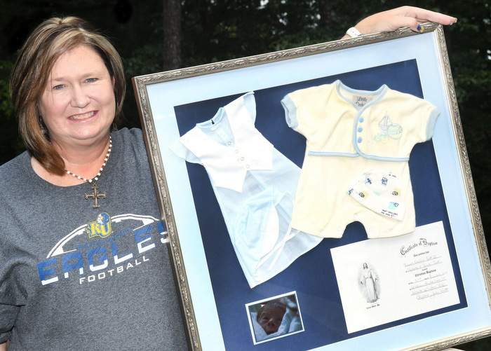 Stephanie Scott holds up the framed clothes from her infant son's baptism. Photo by Rebecca Breyer