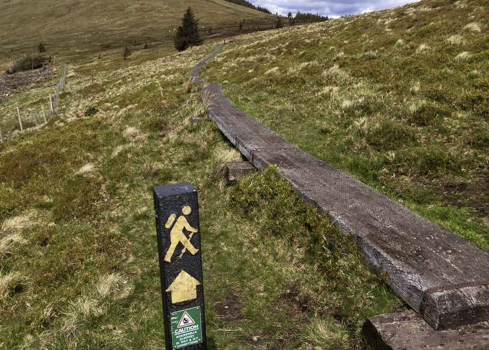 A marker signals the Wicklow Way trail through the Wicklow Mountains in between Glenmalure and Glendalough. The trail takes hikers across boardwalks, on paved busy roads, through part of the national park, on private farm fields and over old logging roads.